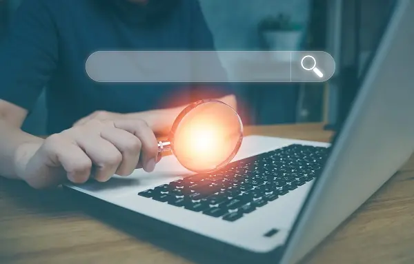 A person holding a laptop and a magnifying glass searching for affiliate programs online.